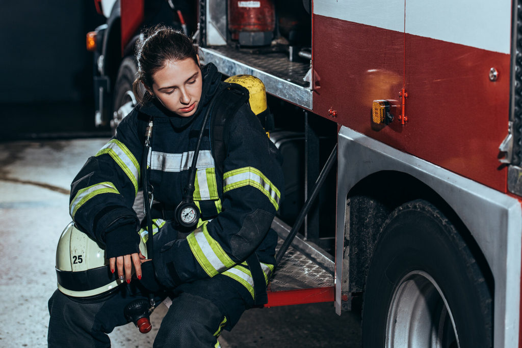 Female firefighter sits on the running board of the fire truck looking stressed. First responders are at a higher risk of developing PTSD. Learn what PTSD is with our online therapist in Ohio and our online therapist in Kentucky.