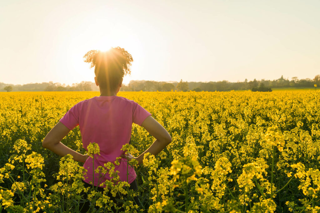 African-American woman standing in a field of flowers staring into the distance. Online Therapy can help you understand the trauma associated with PTSD symptoms. Learn more here.