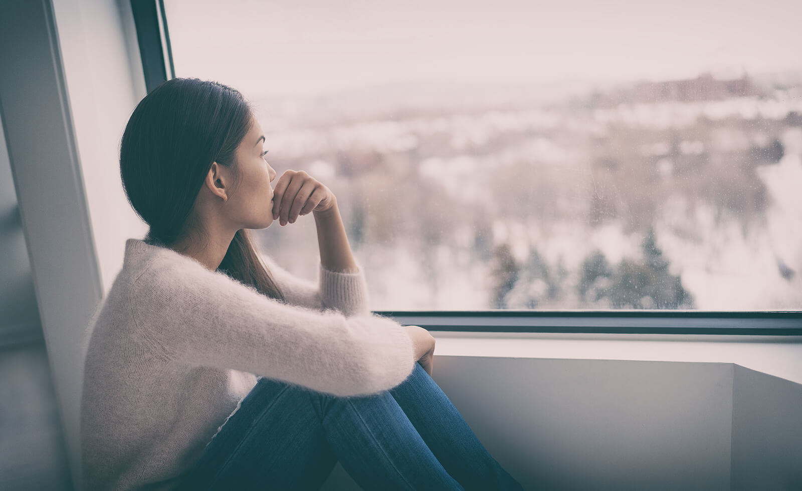 Young woman sitting by a window looking out pensively. PTSD treatment does not have to be scary. Our online PTSD therapist in Ohio is here to gently guide you through the process.