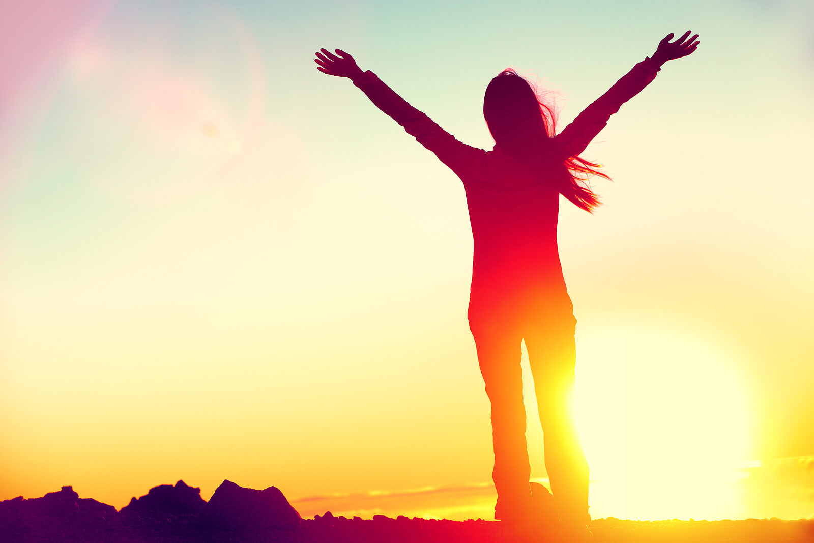 Woman standing on a hill at sunset with her arms raised triumphantly above her head in celebration of success. There is a light at the end of the tunnel. Our trauma therapists in Kentucky can help get you there!