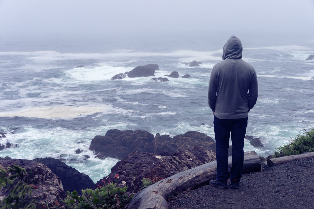 Man standing on the shoreline on a cloudy rainy day looking pensively at the water. Don't let PTSD overtake your life. Reach out to our trauma therapist in Kentucky and get started on your journey to wellness.