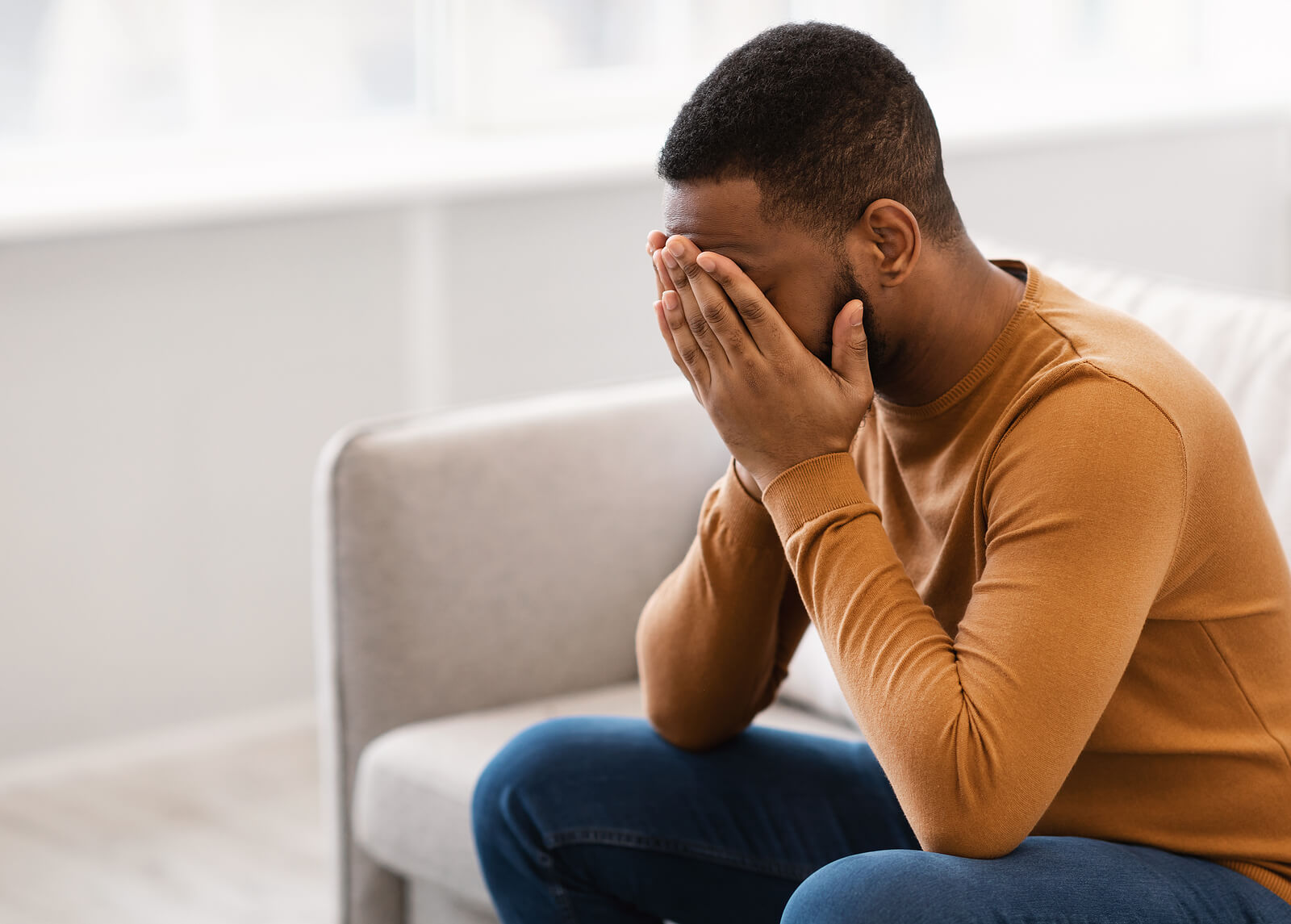 African-American male sits on couch with head in hands. PTSD can be all consuming in your life. Regain control with cognitive processing theory in Ohio.