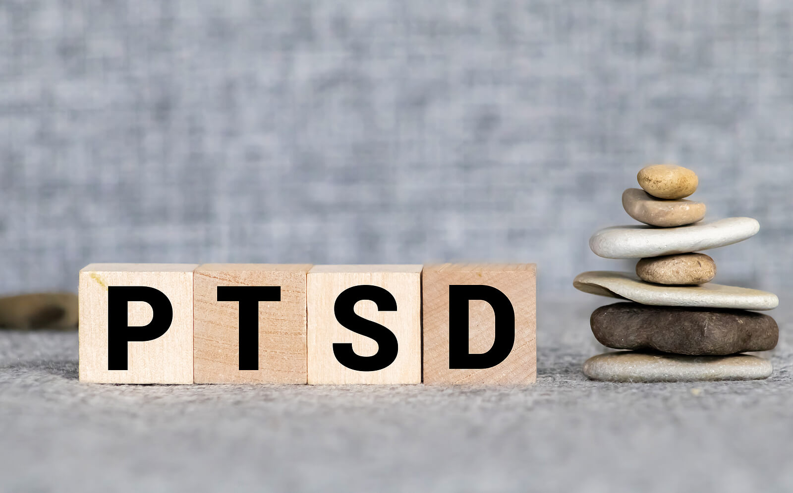 Tiles spell out PTSD next to a stack of small rocks. PE therapy is shown to help treat PTSD effectively. Prolonged exposure therapy in Ohio is available to help!