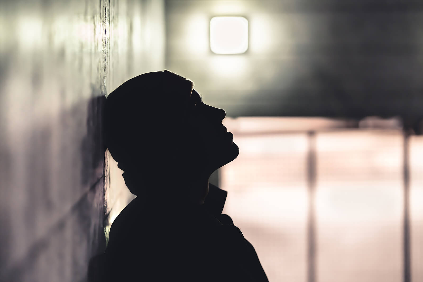 Silhouette of young man in a darkened hallway with his head leaning back against the wall representing the darkness we can live in when shame over past trauma controls us. Trauma-Focused Therapy Services in Ohio can help bring you into the light.