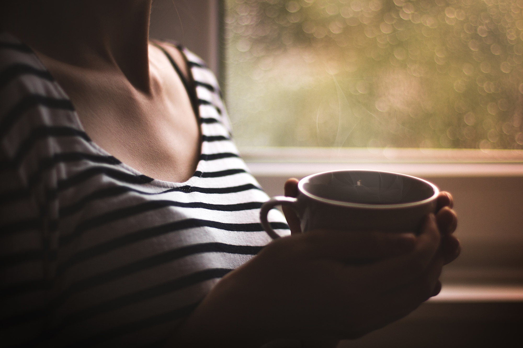 Woman holding a cup of tea looking out the window representing someone contemplating past childhood trauma and the need to address it through Therapy for Childhood Trauma Survivors in Ohio to move forward in life.