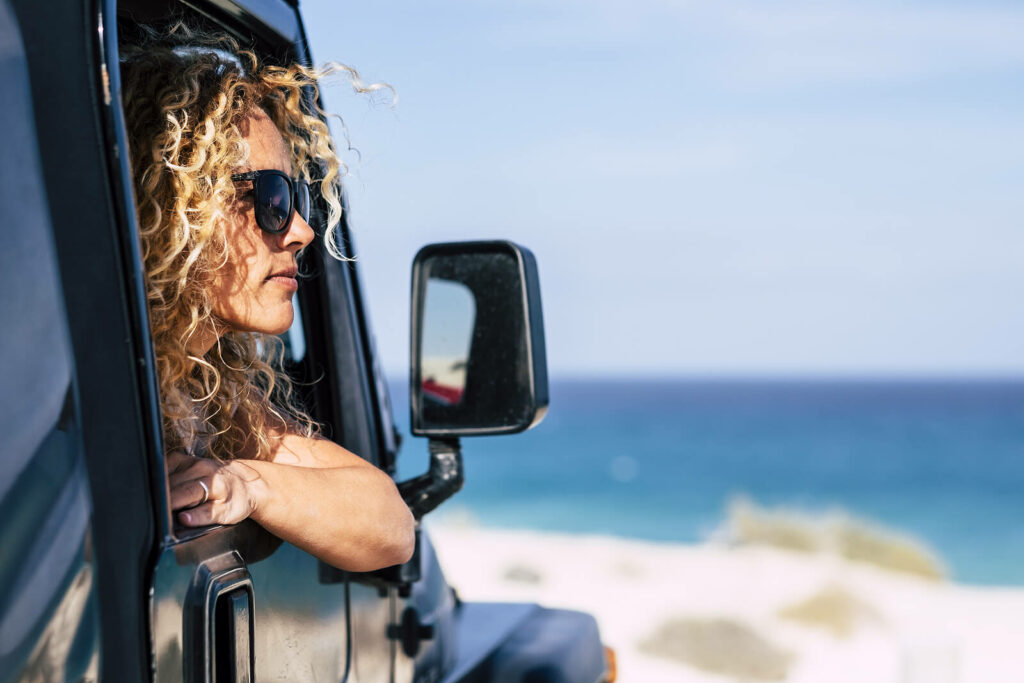 A woman looks out the window of her jeep while parked on the beach representing someone who has found contentment through Online PTSD Treatment in Ohio, Kentucky, and New York. 