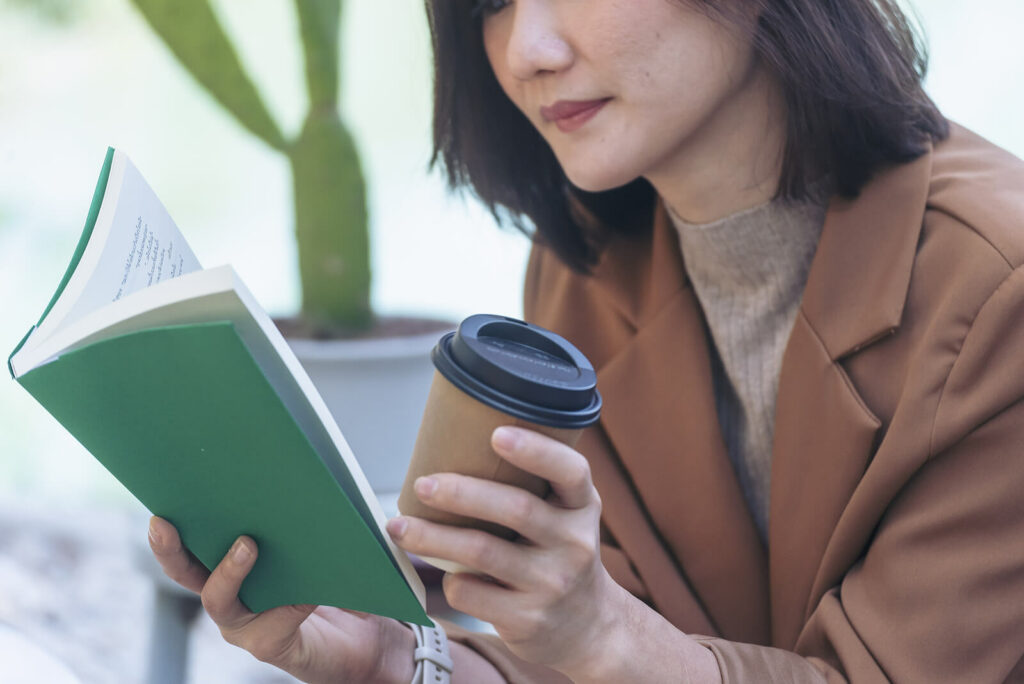 A young Asian woman relaxes with coffee and a book representing someone who has found healing through Therapy for Sexual Assault Survivors in Ohio.