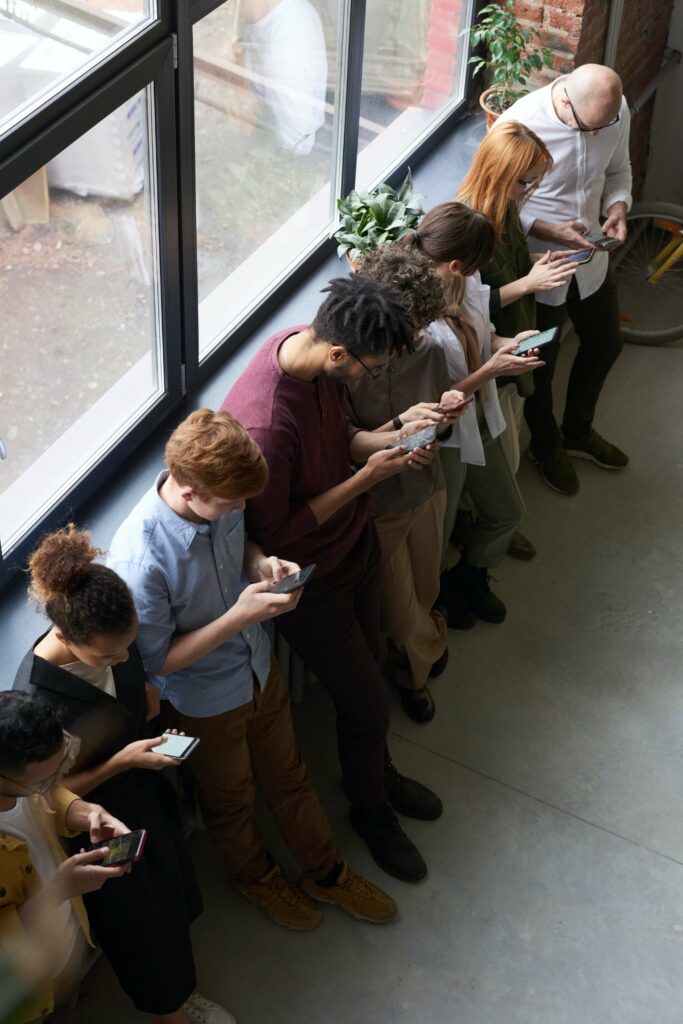 A large group of people all stand next to each other staring at their phones representing society's reliance on social media to self-diagnose our issues. Reach out to a trained Trauma Therapist in Ohio to get professional support and guidance.