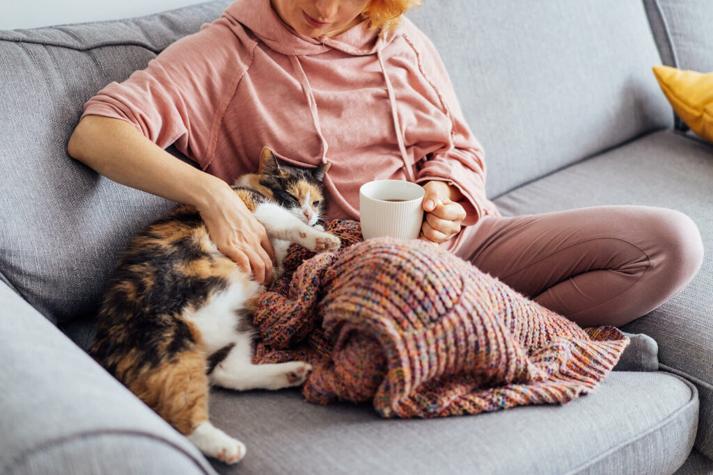 A woman find s comfort sitting on her couch with her cat and a cup of coffee while she deals with survivors guilt after losing a loved one to suicide. PTSD Treatment in Ohio can help you break the cycle of guilt and anger.
