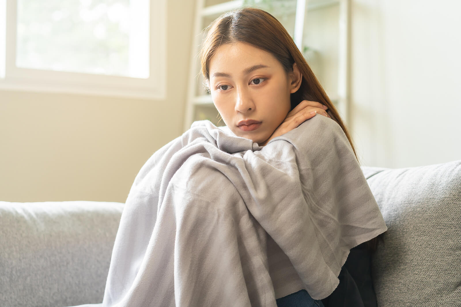 A young woman sits wrapped in a blanket while she struggles to overcome the loss of a loved one to suicide. Get the support you need to find peace after suicide with PTSD Treatment in Ohio.