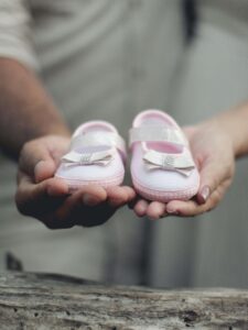 A close-up of two hands gently holding pink baby shoes, symbolizing loss and remembrance. This image reflects the emotional depth explored in survivors guilt in Ohio and highlights the support offered by a grief counselor in Ohio and trauma-focused therapy services in Ohio. 