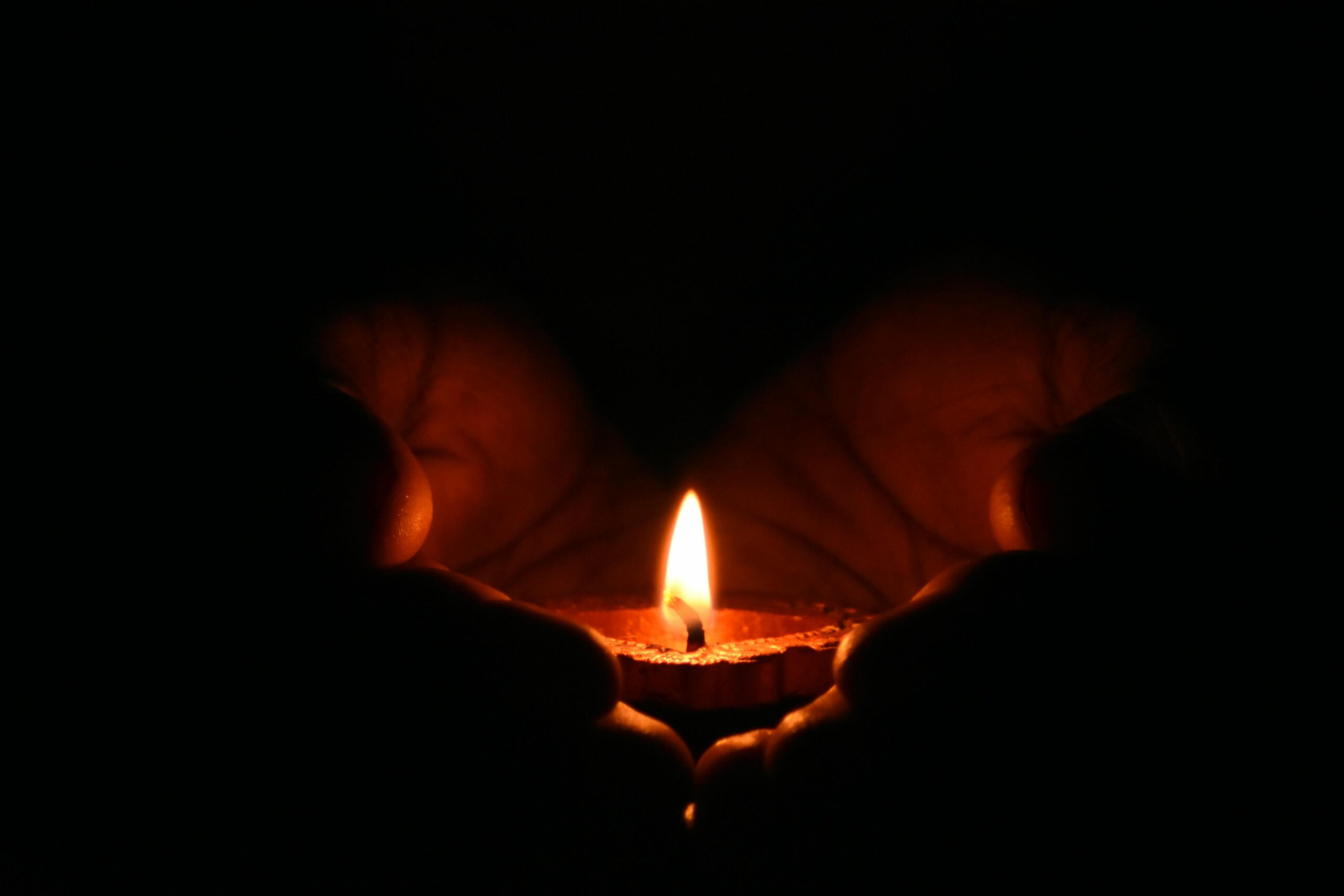 A warm candle flame cradled in hands in a dark space, representing hope and healing during grief. This image is meaningful for those seeking grief counseling in Ohio, coping with survivors guilt in Ohio, or working with a trauma therapist in Ohio.