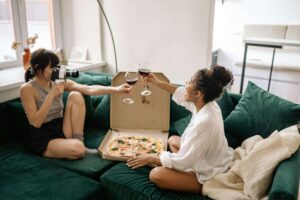 Two women share wine and pizza on a cozy couch, symbolizing healing and connection for a sexual assault survivor in Kentucky, therapy for sexual assault in Kentucky, and support from a therapist for sexual trauma in Kentucky. 