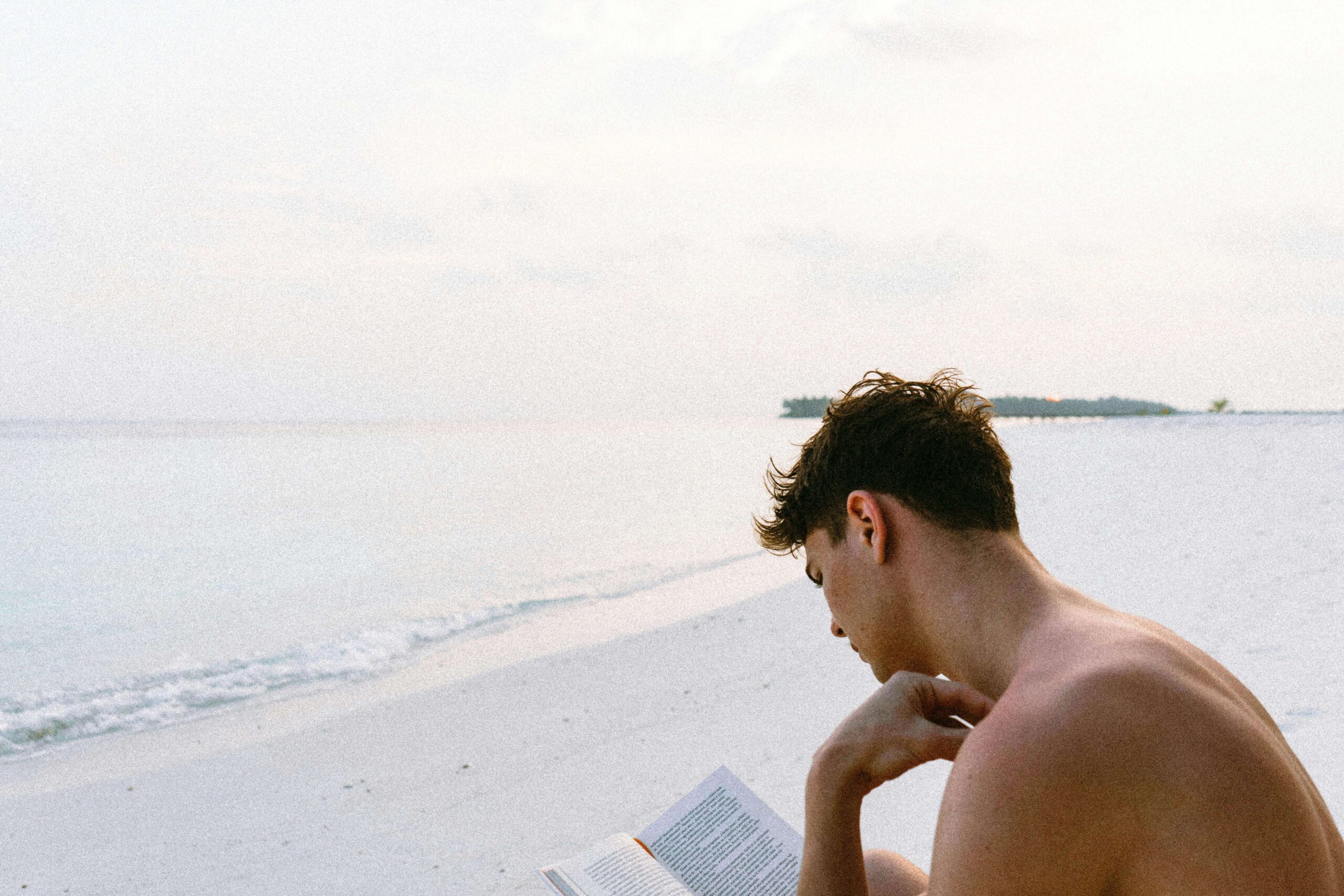 A young man reads on a serene beach, representing reflection and personal healing through therapy for sexual assault in Kentucky, sexual assault survivor in Kentucky, and guidance from a therapist for sexual trauma in Kentucky.