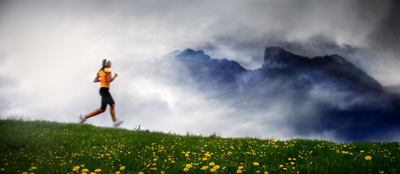 A woman runs through a green field beneath foggy mountains, symbolizing hope and resilience supported by therapy for childhood trauma survivors, a trauma therapist in ohio, and trauma-focused therapy services in ohio.