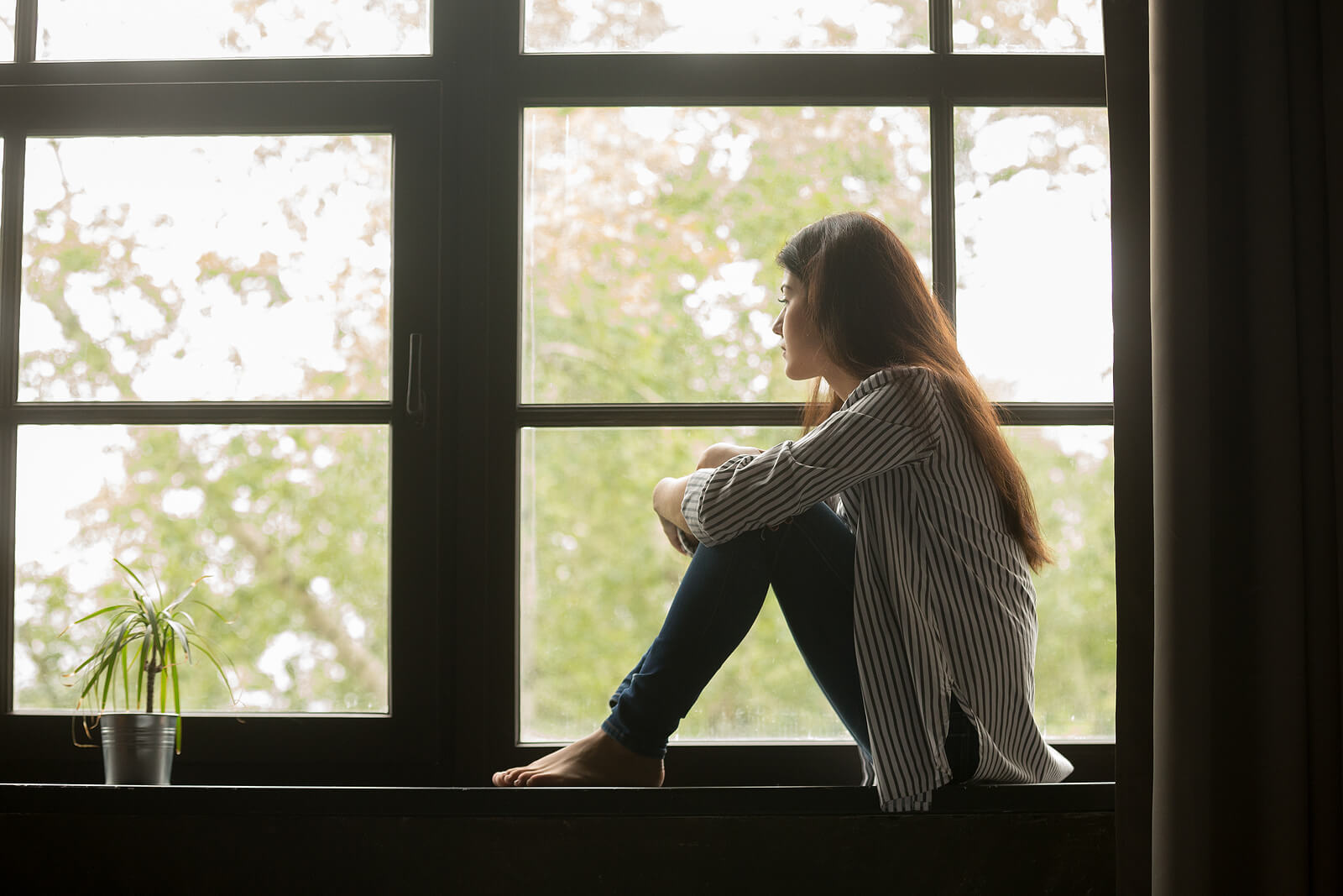 A woman sits curled up on a windowsill gazing outside, reflecting the quiet isolation and internal weight that PTSD symptoms in Ohio can create long after trauma has occurred. The cycle of shame often keeps survivors locked in silence, unable to move forward without the right support. Working with a PTSD therapist in Ohio can help survivors finally begin to separate who they are from what happened to them.