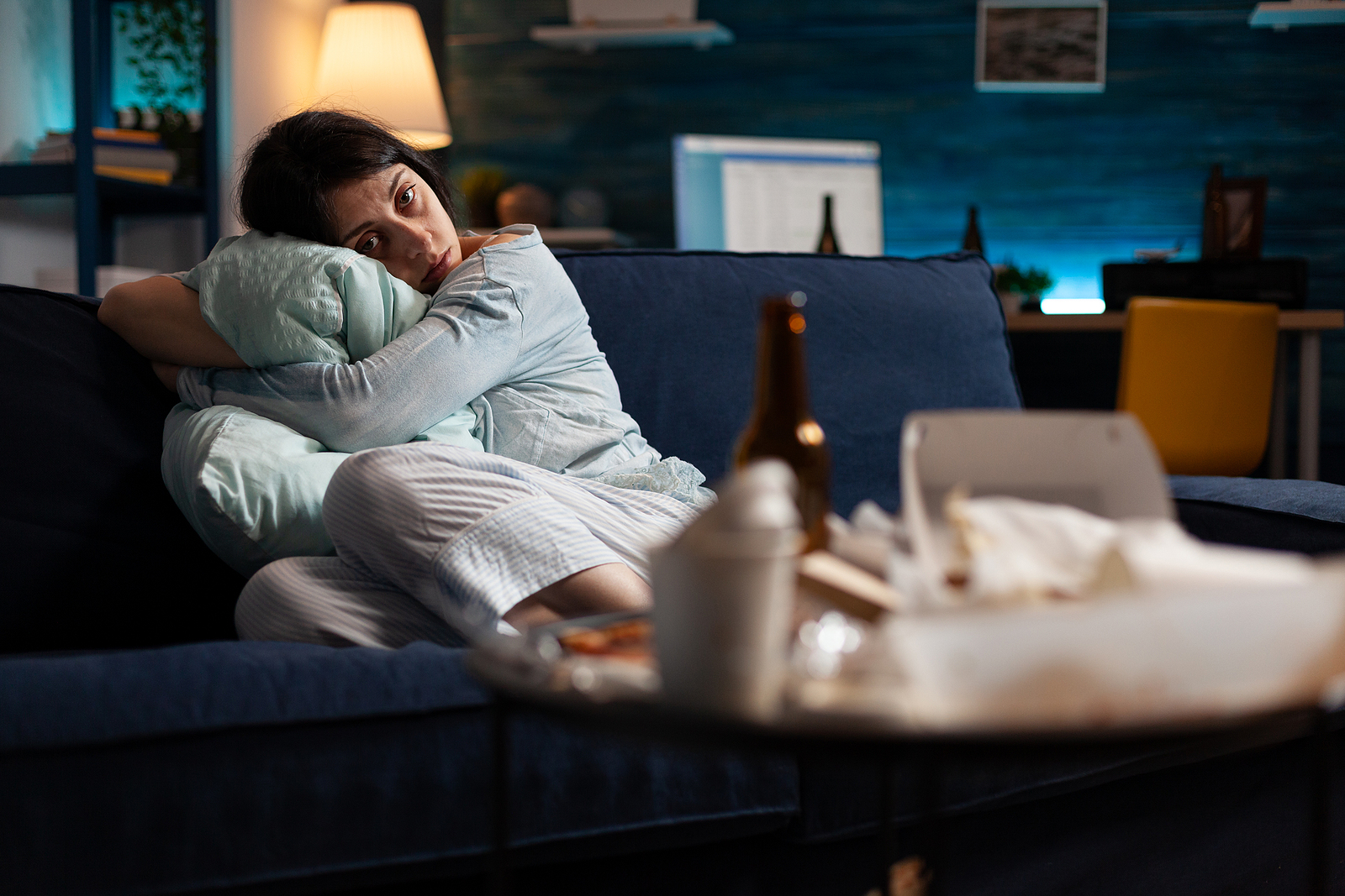 A woman sits curled up on a dark couch hugging a pillow, surrounded by empty bottles and takeout containers, powerfully depicting the isolation and heaviness of the cycle of shame that trauma survivors so often carry alone. This kind of quiet, invisible suffering is exactly what a trauma therapist in Cincinnati, OH is trained to recognize and compassionately address. Trauma-focused therapy services in Ohio and online trauma counseling offer a safe, supportive path toward healing for those who feel too weighed down to take the first step.