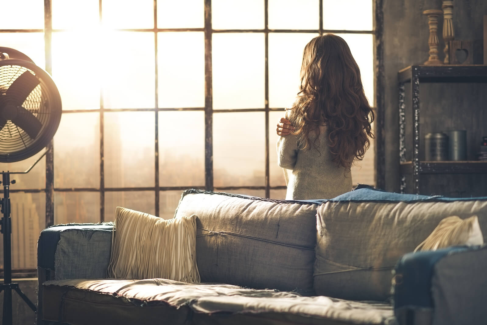 A woman stands facing a sunlit window with her arms wrapped around herself, a quiet image of the vulnerability many sexual assault survivors in Ohio feel in the days after trauma. Therapy for sexual assault survivors and a therapist for sexual trauma in Ohio can help her feel safe again.